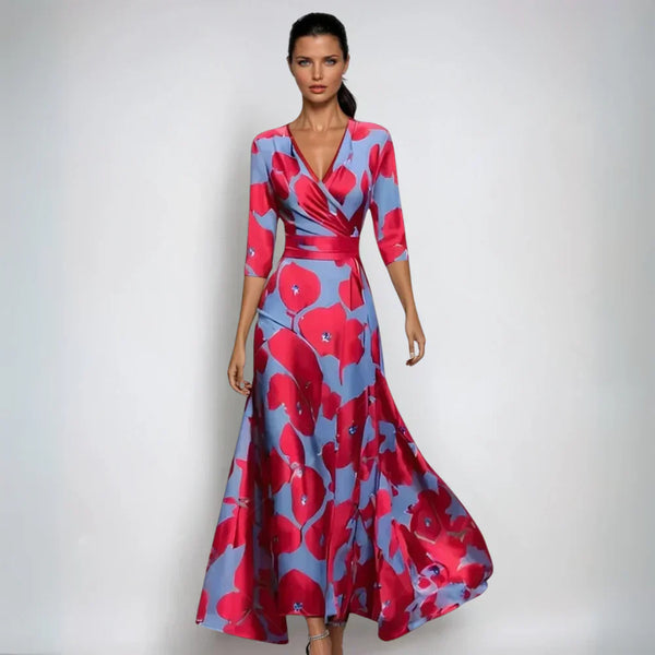 Robe longue élégante à motifs floraux rouges et bleus, manches trois-quarts, portée par une femme sur fond neutre. Mode féminine chic et tendance.