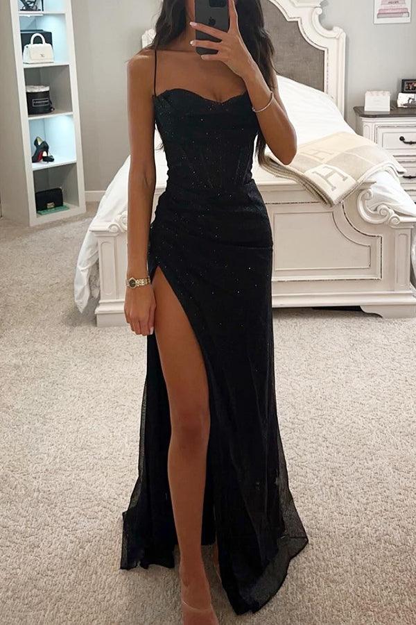 Femme en robe de soirée noire élégante avec fente haute, posant devant un miroir dans une chambre moderne. Mode, glamour, tenue de soirée.