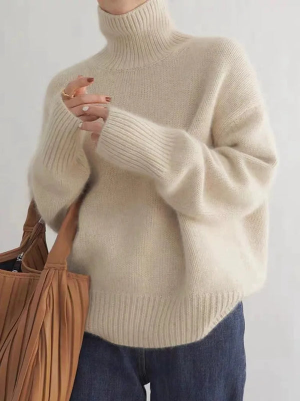 Femme portant un pull en laine beige à col roulé, manches longues, avec un sac en cuir marron, sur fond neutre. Mode automne-hiver élégante.