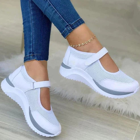 Chaussures de sport blanches pour femmes avec sangle, semelle épaisse et design en maille respirante, portées avec un jean bleu.