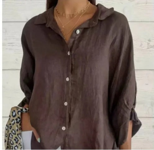 Chemise en lin marron pour femme, manches retroussées, col ouvert, boutons blancs, collier doré, fond en bois clair. Mode décontractée élégante.