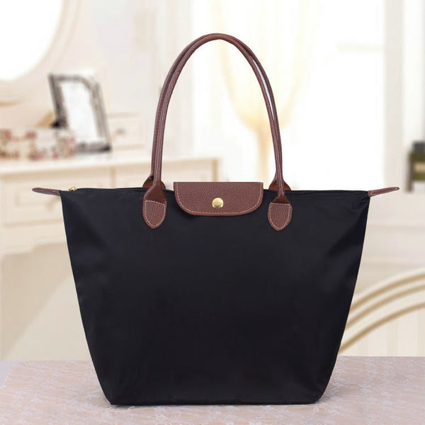 Sac à main noir élégant avec poignées marron en cuir, posé sur une table. Accessoire mode femme, design classique, idéal pour le quotidien.