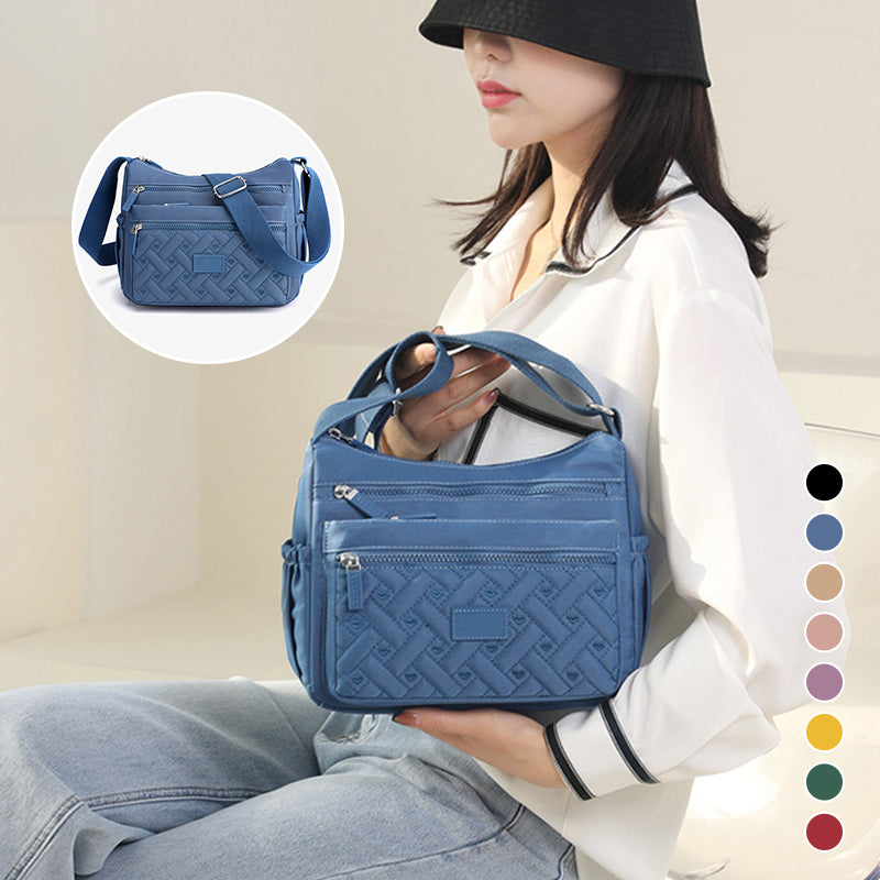 Sac à main bleu en cuir avec motif tressé, porté par une femme. Design élégant, multiple poches zippées. Accessoire mode tendance et pratique.