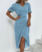 Robe bleue à motifs floraux blancs, manches courtes bouffantes, col en V, longueur mi-mollet, portée par une femme sur fond blanc.