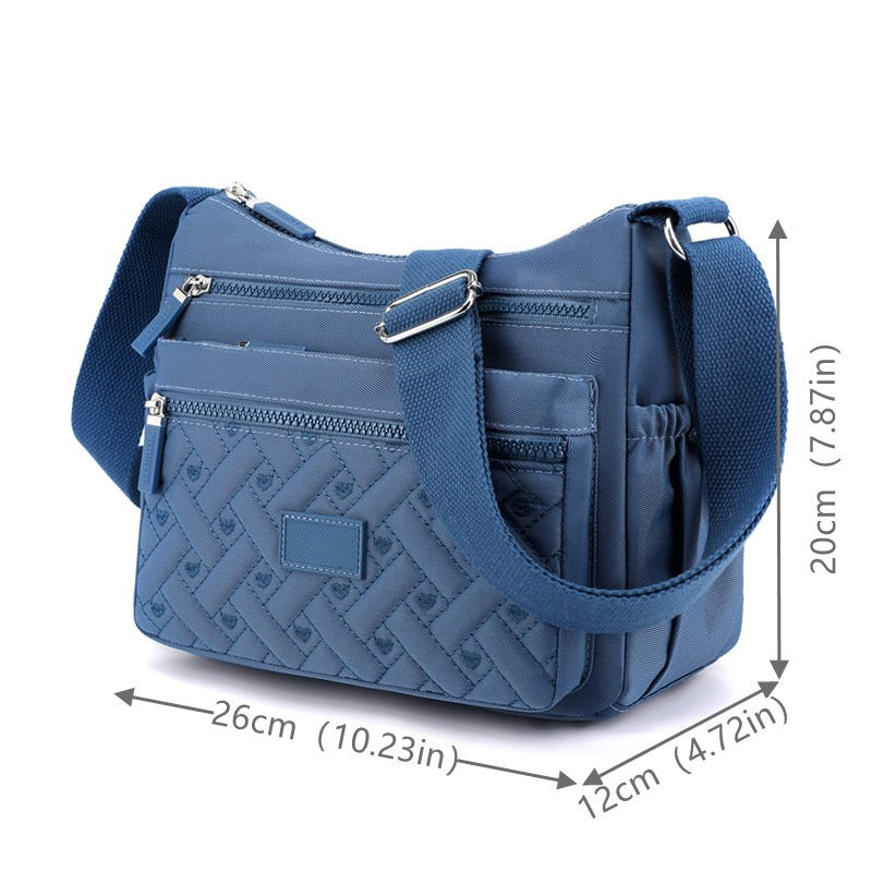 Sac bandoulière bleu en nylon avec motifs tressés, poches zippées, bandoulière ajustable. Dimensions: 26x12x20 cm. Accessoire mode pratique.
