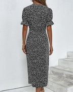 Robe longue à fleurs noires et blanches, manches courtes bouffantes, femme de dos, style élégant, mode estivale, fond blanc minimaliste.