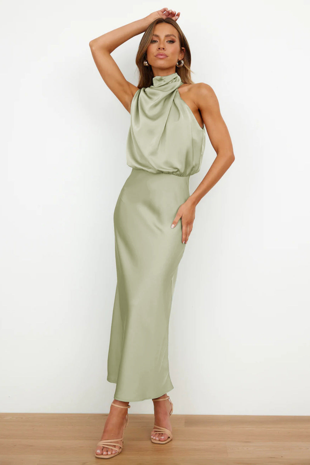 Robe longue satinée vert sauge, col drapé, sans manches, portée par une femme posant élégamment. Mode féminine chic et tendance.