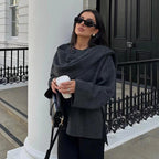 Femme élégante en manteau gris, lunettes de soleil noires, tenant un café devant une maison blanche. Mode automne, style urbain chic.