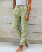 Pantalon en lin vert clair pour femme, taille élastique avec cordon, poches latérales, style décontracté, fond en bois clair.