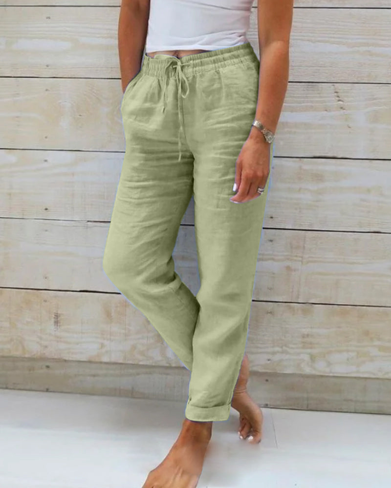 Pantalon en lin vert clair pour femme, taille élastique avec cordon, poches latérales, style décontracté, fond en bois clair.