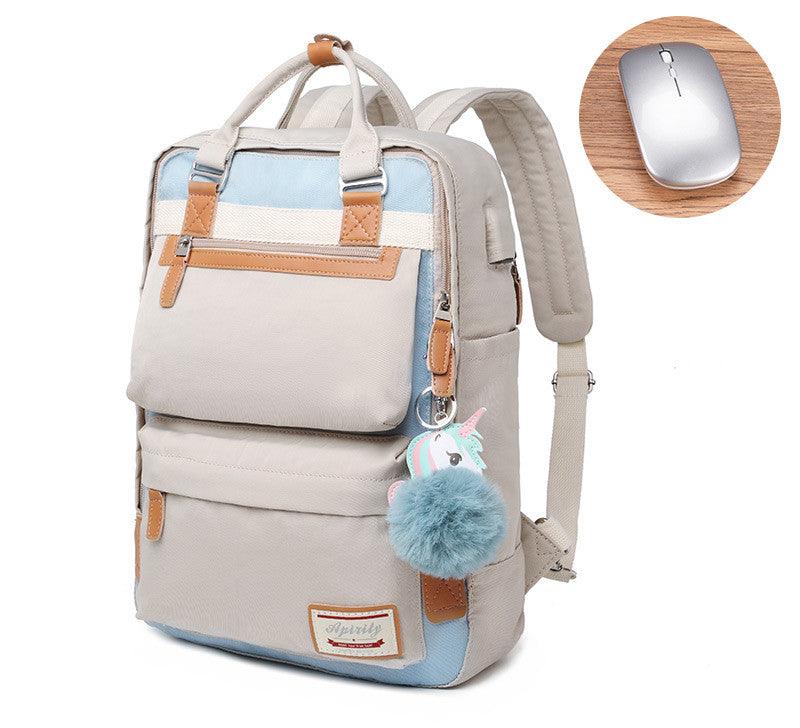 Sac à dos beige et bleu avec pompon licorne, poches multiples, détails en cuir marron, à côté d'une souris sans fil grise sur une table en bois.
