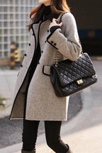 Femme portant un manteau gris élégant avec boutons noirs, sac à main matelassé noir à chaîne dorée, tenue chic automne-hiver, mode urbaine.