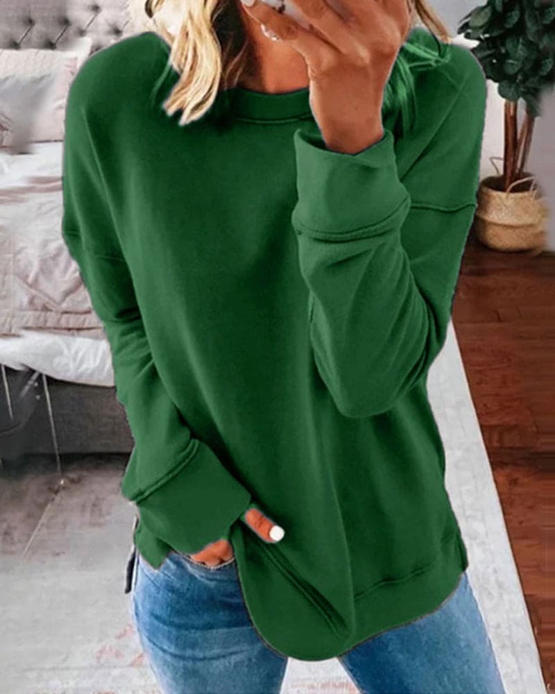 Femme portant un pull vert ample, manches longues, avec un jean bleu, dans une chambre moderne. Mode décontractée, tendance automne-hiver.