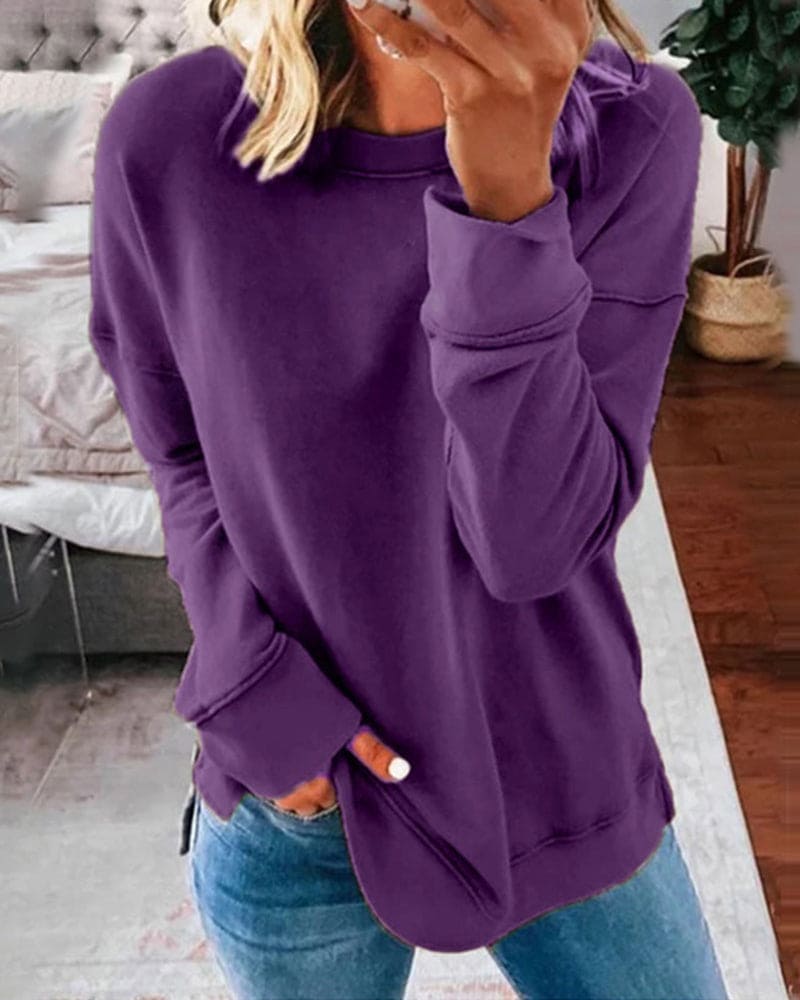 Femme portant un pull violet ample, tenant un smartphone, debout dans une chambre moderne. Mode décontractée, style automne-hiver.