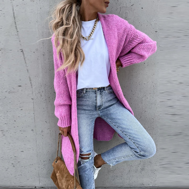 Femme portant un cardigan rose, t-shirt blanc, jeans déchirés, et sac marron. Mode décontractée, tendance automne, style urbain chic.