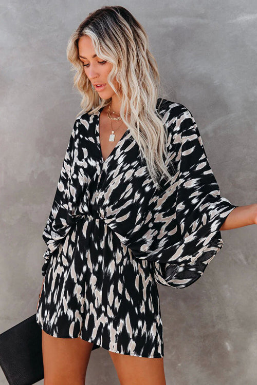 Femme en robe kimono noire et blanche à motifs abstraits, cheveux blonds ondulés, tenant une pochette noire. Mode élégante et tendance.