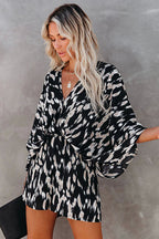 Femme en robe kimono noire et blanche à motifs abstraits, cheveux blonds ondulés, tenant une pochette noire. Mode élégante et tendance.