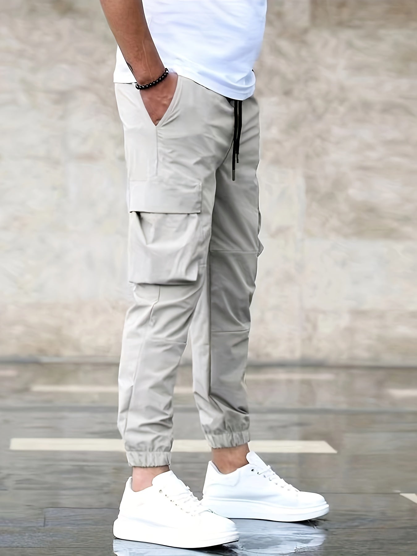 Pantalon cargo beige pour homme avec poches latérales, porté avec des baskets blanches et un t-shirt blanc, style décontracté moderne.