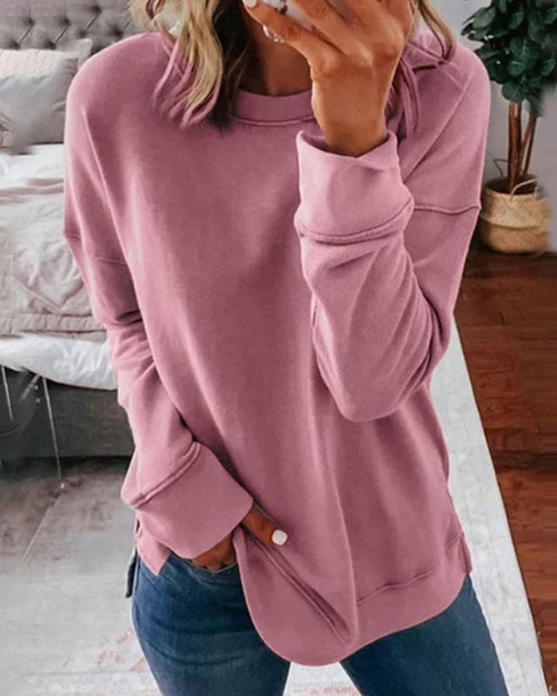 Femme portant un pull rose décontracté, manches longues, dans une chambre moderne. Mode féminine, style confortable, tenue quotidienne.