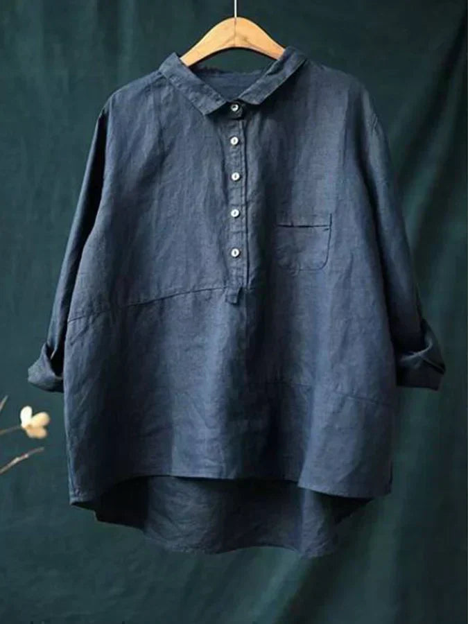 Chemise en lin bleu foncé sur cintre en bois, manches longues, col boutonné, poche poitrine, fond vert. Mode éco-responsable, style décontracté.