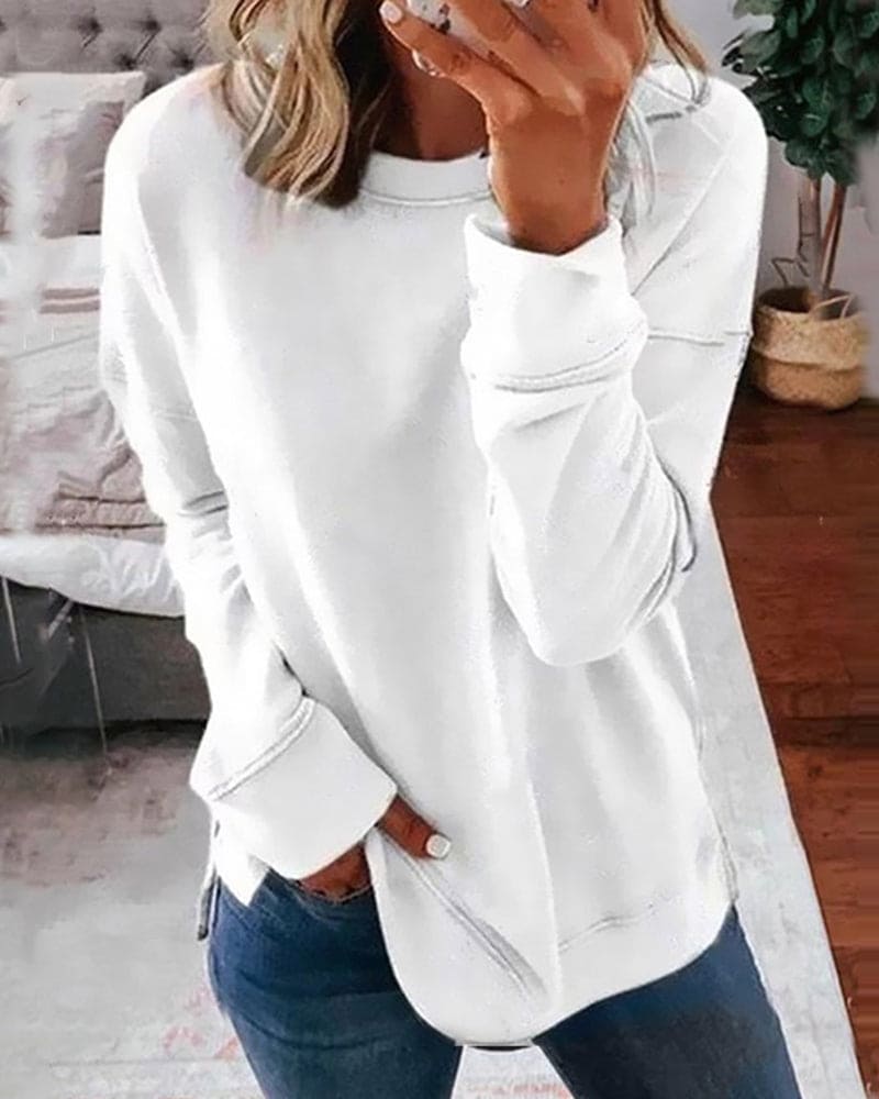 Femme portant un pull blanc décontracté, manches longues, dans un intérieur moderne. Mode automne, style confortable, tendance casual chic.