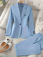 Costume bleu clair élégant pour femme, avec veste à deux boutons et pantalon assorti, posé sur un canapé beige. Chaussures blanches et sac à main inclus.
