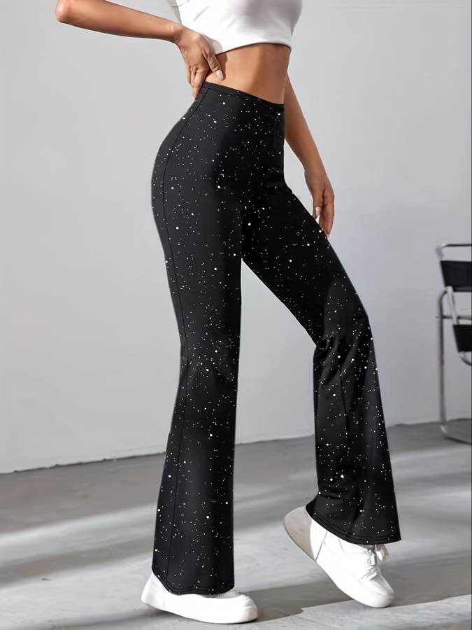 Pantalon évasé noir à motifs étoilés, porté par une femme, associé à un haut blanc court et des baskets blanches, style moderne et décontracté.