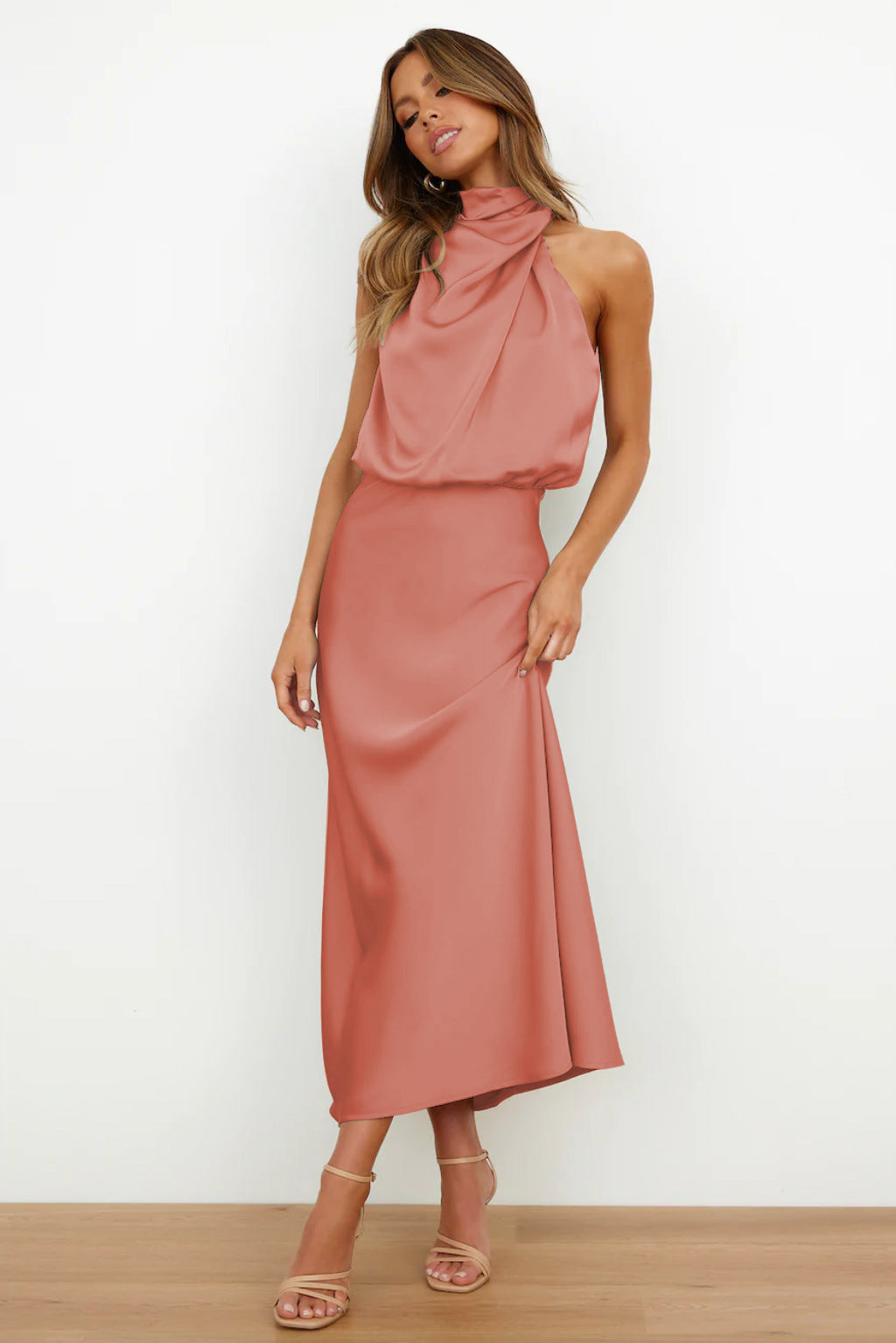 Robe longue rose saumon élégante, sans manches, col drapé, portée par une femme. Mode féminine chic, tenue de soirée tendance.