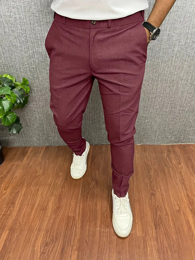 Pantalon bordeaux homme élégant, coupe ajustée, porté avec des baskets blanches, sur fond de sol en bois et mur gris, style moderne et décontracté.