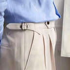 Chemise bleue élégante rentrée dans un pantalon beige à plis avec ceinture ajustable, style chic et moderne pour homme.