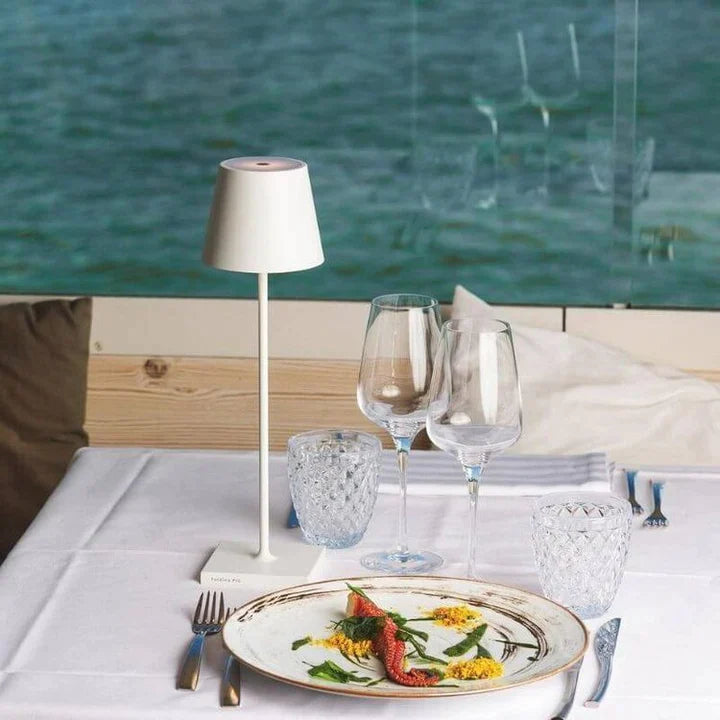 Assiette gastronomique avec poisson et légumes sur table élégante, vue sur mer, verres à vin, ambiance restaurant chic, bord de mer.