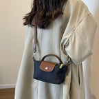 Sac à bandoulière noir et marron porté par une femme en manteau beige. Accessoire mode élégant, tendance automne, style chic et pratique.
