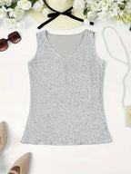 Débardeur argenté à paillettes, col en V, entouré d'accessoires d'été : lunettes de soleil, chapeau, fleurs blanches, chaussures beiges et sac à main.