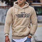 Homme portant un sweat à capuche beige en peluche avec l'inscription "Invest in Yourself", mode décontractée, style urbain, jeans déchirés.