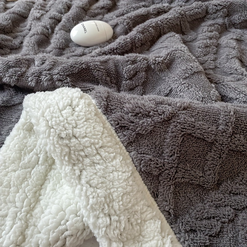 Couverture en fausse fourrure grise et blanche avec motif géométrique, posée sur un lit, accompagnée d'un flacon de parfum Chanel.