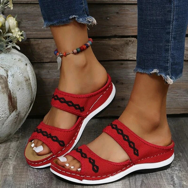 Sandales rouges pour femme avec semelle blanche, ornées de motifs noirs, portées avec un jean déchiré. Mode estivale, chaussures confortables.