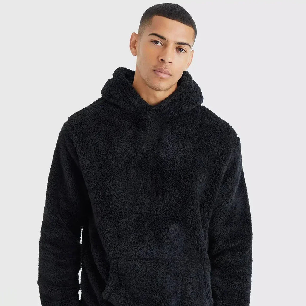Jeune homme portant un sweat à capuche noir en peluche, style décontracté, sur fond blanc. Mode masculine, confort, tendance automne-hiver.