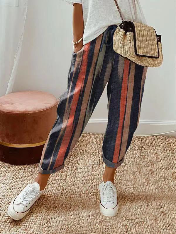 Pantalon rayé multicolore femme, style décontracté, avec sac à main en paille et baskets blanches, sur tapis beige. Mode tendance et confortable.