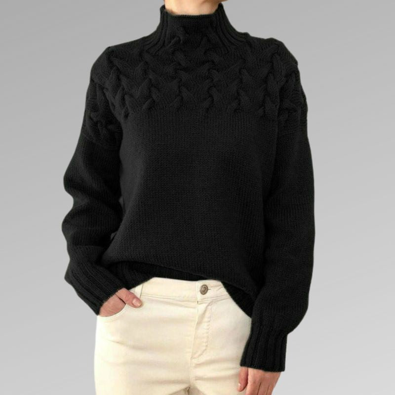 Pull noir en laine torsadée pour femme, col montant, manches longues, porté avec un pantalon beige. Mode hiver élégante et confortable.