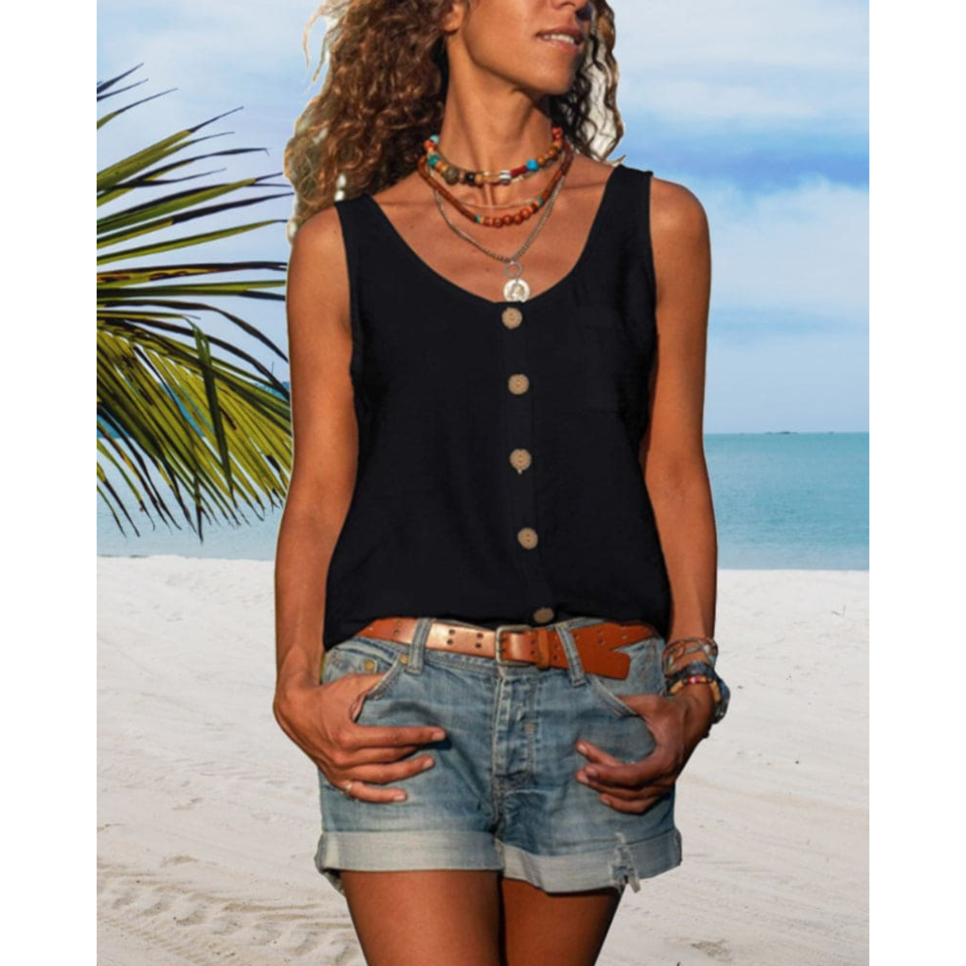 Femme en débardeur noir à boutons, short en jean, sur plage tropicale. Colliers colorés, ciel bleu, mer en arrière-plan. Mode estivale décontractée.