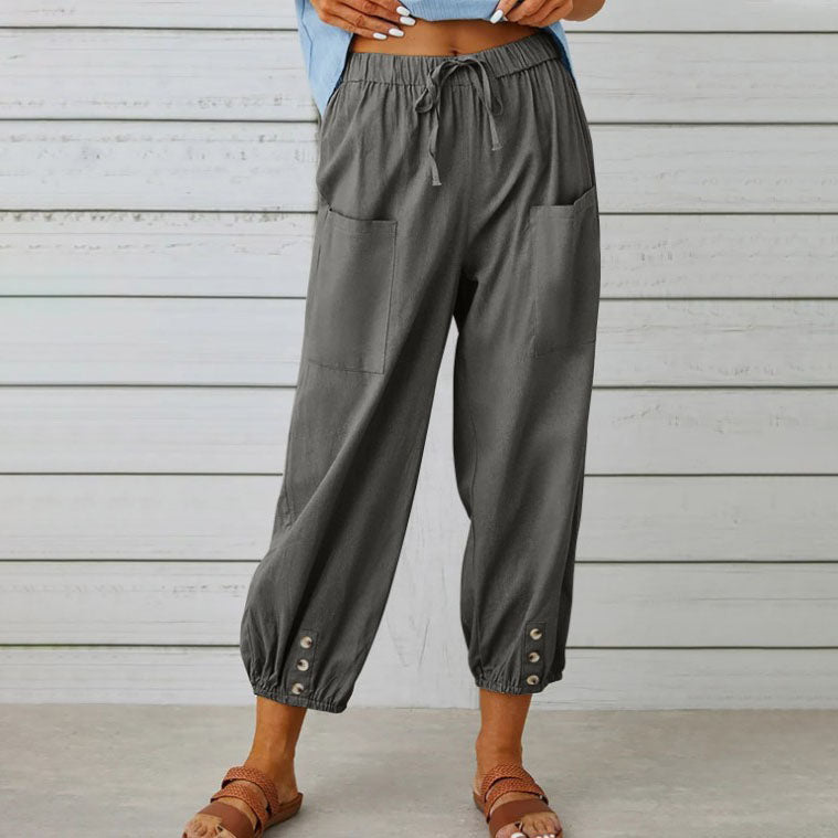 Pantalon ample gris pour femme avec poches avant, taille élastique et boutons décoratifs, style décontracté, fond en bois clair.