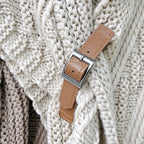 Ceinture en cuir marron avec boucle argentée posée sur un pull en tricot beige texturé. Accessoire mode élégant et tendance.