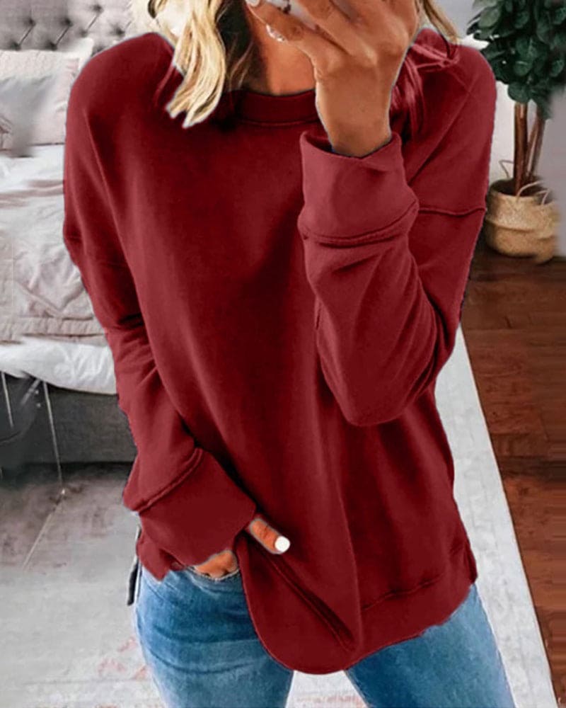 Femme portant un pull rouge ample, manches longues, avec un jean bleu, dans une chambre moderne. Mode décontractée, style automne-hiver.