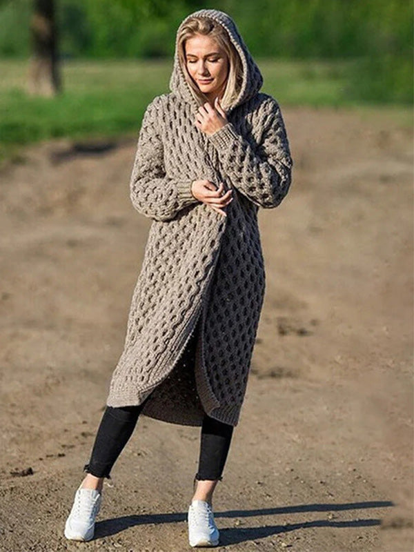 Femme portant un long cardigan à capuche en tricot beige, motif torsadé, sur un chemin de terre, style décontracté, mode automne-hiver.