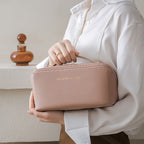 Femme tenant une élégante trousse de toilette rose en cuir, inscription dorée, sur fond de flacon décoratif. Accessoire mode chic et pratique.