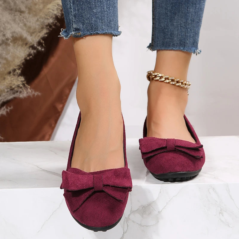Chaussures ballerines bordeaux avec nœud, portées avec un jean effiloché. Accessoire bracelet de cheville doré. Mode féminine élégante.