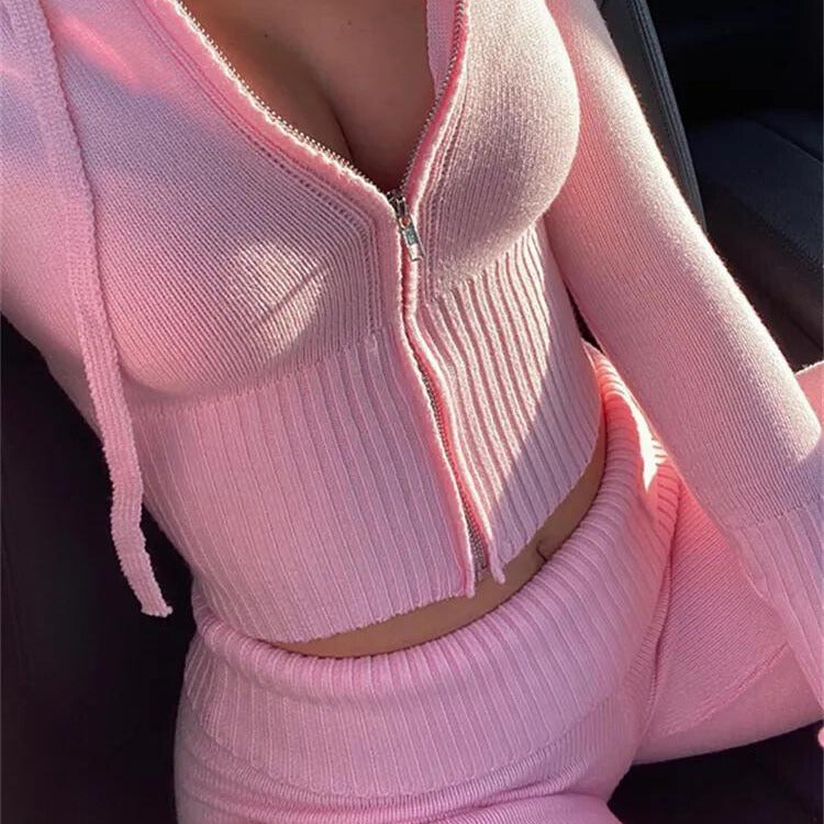 Femme portant un ensemble rose en tricot, composé d'un haut à capuche zippé et d'un pantalon assorti, assise dans une voiture. Mode féminine tendance.