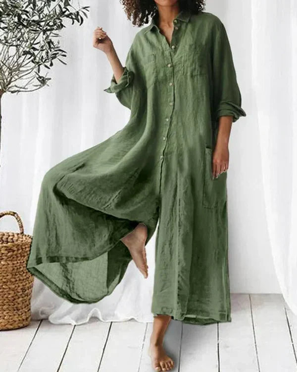 Robe longue en lin vert olive, manches longues, style décontracté, portée par une femme pieds nus. Décor minimaliste avec plante en pot.