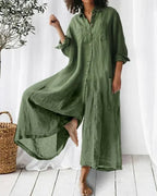 Robe longue en lin vert olive, manches longues, col chemise, poches avant, portée par une femme pieds nus, ambiance décontractée et naturelle.