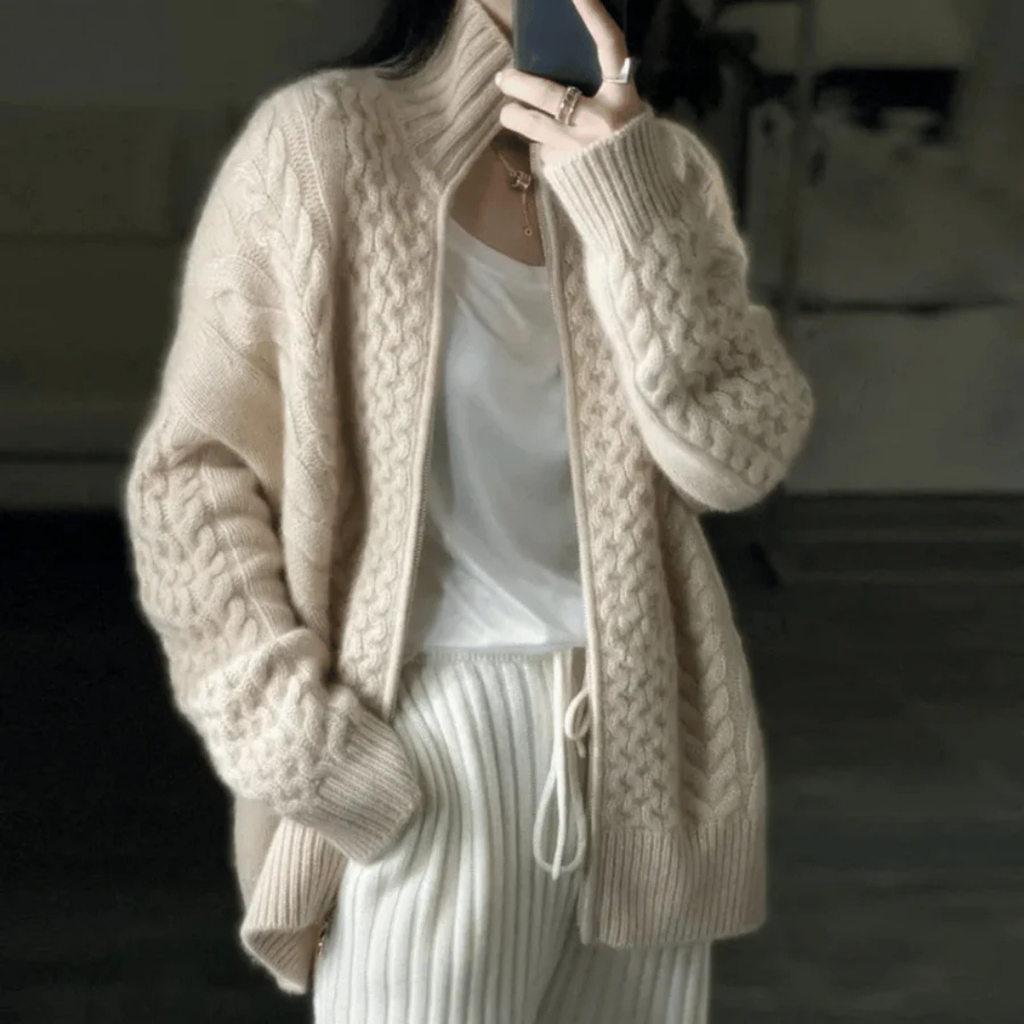 Femme portant un cardigan en laine beige avec motifs torsadés, associé à un t-shirt blanc et un pantalon côtelé. Mode automne-hiver élégante.